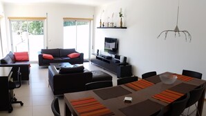A modern living room with a dining area, featuring a large wooden table, black chairs, and a sofa with red cushions. - Beautiful villa for 8 people with private pool close to the beach (São Martinho do Porto)