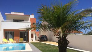 A modern house with a swimming pool, a car parked in the driveway, and a palm tree in the yard. - Beautiful villa for 8 people with private pool close to the beach (São Martinho do Porto)