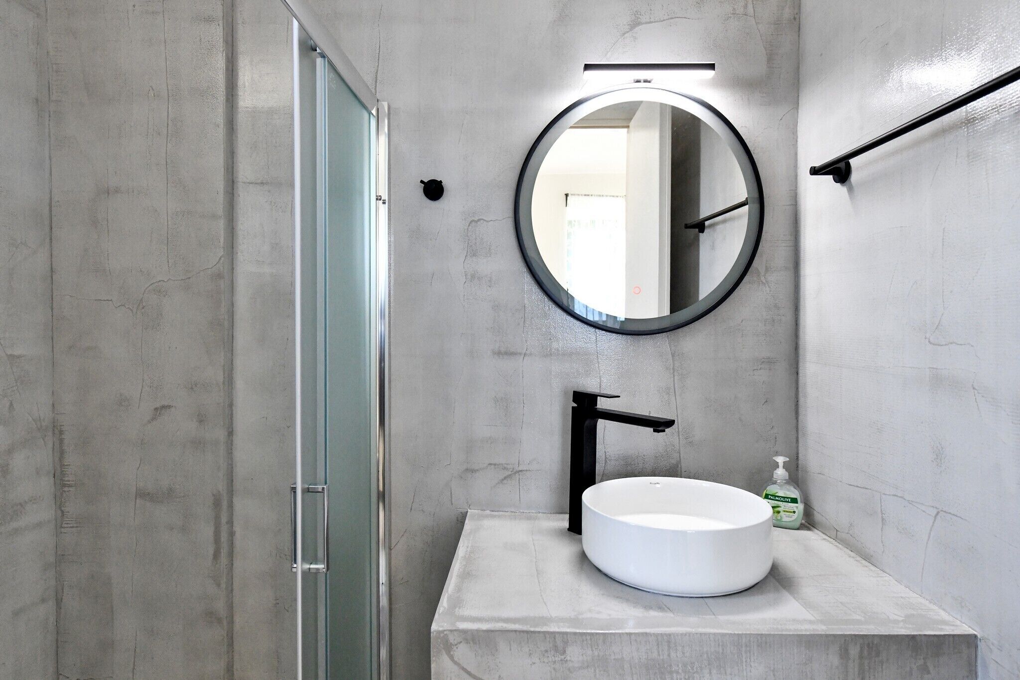 A bathroom with a round mirror, a white sink, and a handheld soap dispenser.