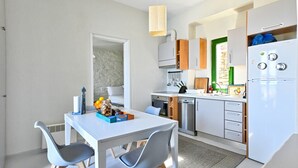 Et kompakt køkken med spiseplads, med et hvidt bord, grå stole og moderne hårde hvidevarer.