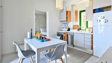 A compact kitchen with a dining area, featuring a white table, grey chairs, and modern appliances.
