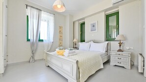 A bedroom with a bed, two bedside tables, a wall clock, and a window with curtains.