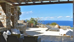 A stone-walled outdoor seating area with lounge chairs and a view of the sea.