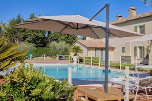 Ein Poolbereich mit Liege, Sonnenschirm und Holztisch.