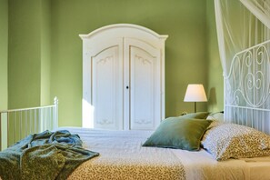 Een slaapkamer met een bed, een witte kledingkast, een nachtkastje met een lamp en een decoratief metalen hoofdbord.