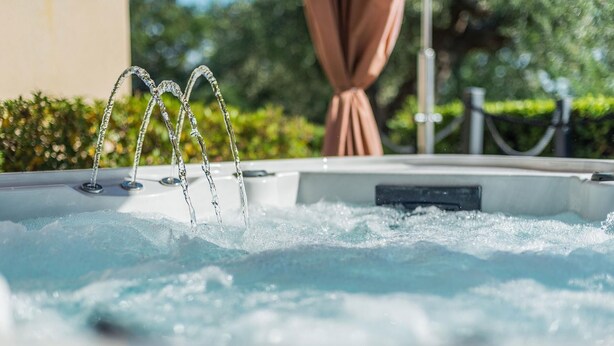 Un bain à remous avec des jets d’eau en mouvement, entouré de verdure et doté d’un espace abrité.