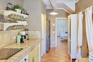 Een keuken met een fornuis, een koffiezetapparaat en een blender. Er is een plank met een plant en een mand.