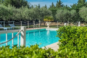 A swimming pool with lounge chairs and a decorative urn, surrounded by greenery and trees.