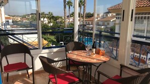 Ein Balkon mit Korbstühlen und einem Tisch, mit Blick auf einen Pool und Palmen.