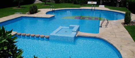 A swimming pool with a tiled deck, surrounded by greenery and residential buildings.