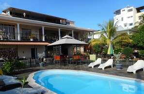 Relax by the pool surrounded by lounge chairs and umbrellas, with a view of the surrounding greenery from the adjacent balcony.