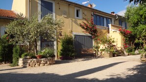 A two-story building with a gravel driveway, a wooden bench, and various potted plants and flowers. - Roussillon Gargas: Mansion - Roussillon (Gargas)