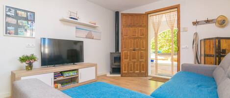 A modern living room with a flat-screen TV, a sofa, a coffee table, and a wooden door leading outside.