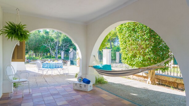 A covered patio with a hammock, seating area, and a view of the garden.