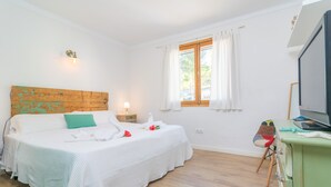 Ein Schlafzimmer mit einem Bett, einem Holzkopfstück, einem Fenster mit Vorhängen, einem Fernseher und einer Kommode.
