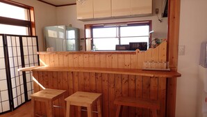 A kitchen with wooden paneling, a window, a refrigerator, and a microwave. - Guesthouse SORA - Hostel (Minamiizu)