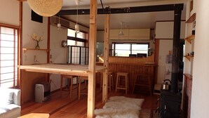 A traditional Japanese-style interior with tatami flooring, a low wooden table, a hanging light fixture, and a black stove. - Guesthouse SORA - Hostel (Minamiizu)