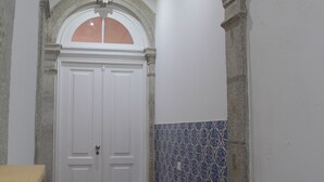 A hallway with a white door, a stone archway, and a tiled wall. - ROMANTIC and light apartment in Oportodowntown with mezzanine. (Porto)