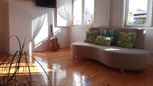 A living room with a curved sofa, a guitar leaning against the wall, and a flat-screen TV mounted above. - ROMANTIC and light apartment in Oportodowntown with mezzanine. (Porto)
