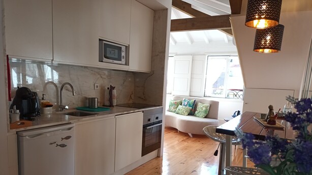 A modern kitchen with white cabinets, a built-in microwave, and a coffee machine. There is a wooden dining table with a vase of flowers. - ROMANTIC and light apartment in Oportodowntown with mezzanine. (Porto)