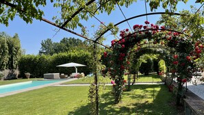 Ein Garten mit Swimmingpool, einer überdachten Terrasse und einem Rosenbogen.