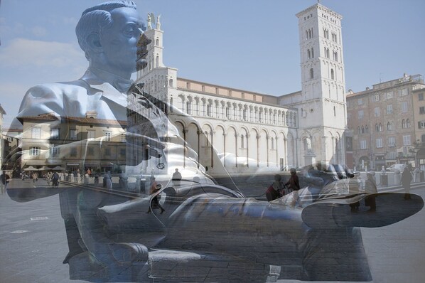 A large statue in a public square with a historic building in the background.