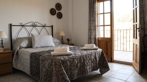 A bedroom with a bed, two bedside tables with lamps, a window with curtains, and a door leading to an outdoor area. - Piltraque - our holiday country villa to rent in the Spanish Coutryside (Riogordo)