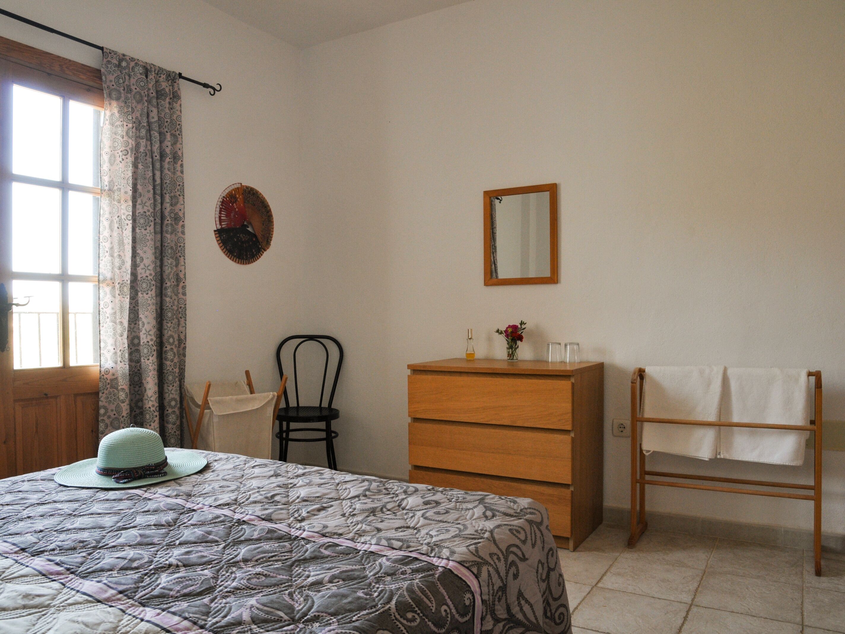 A bedroom with a bed, a dresser, a chair, a mirror, and a window with curtains.