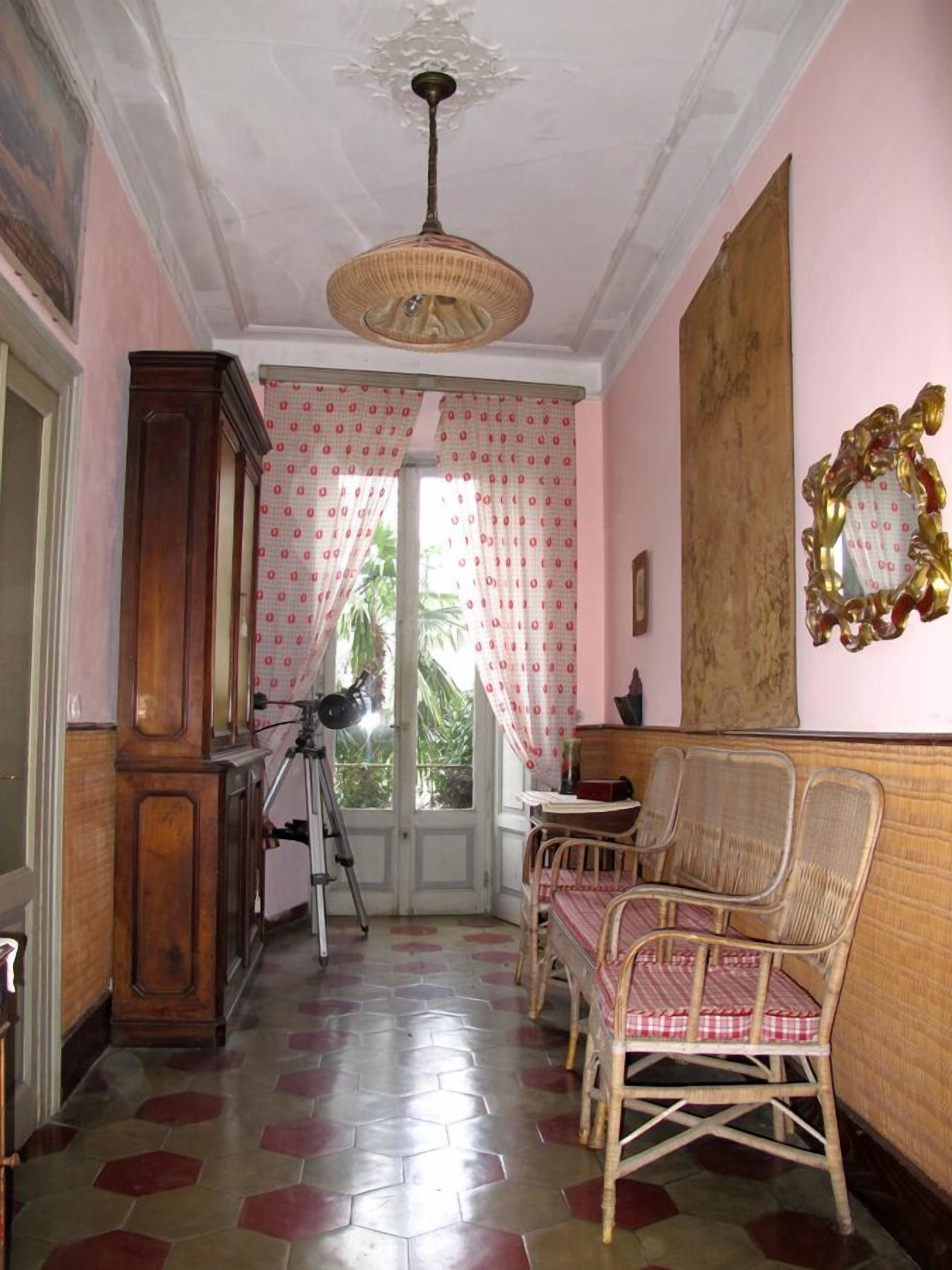 A room with a wooden cabinet, a tripod, wicker chairs, a table, and a large mirror on the wall.