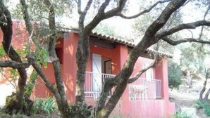 Um pequeno edifício vermelho com varanda, cercado por árvores e vegetação.