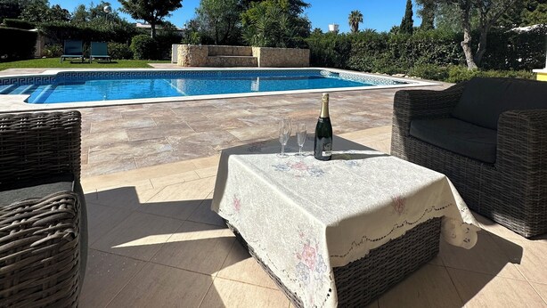 An outdoor patio area with a pool, wicker furniture, and a table with a bottle and glasses. - Beautiful 4 bedroom villa in the Alto Golf (ALVOR)