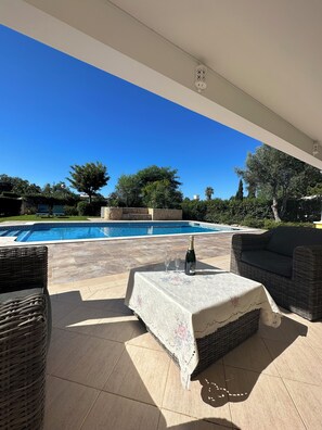 Ein Außenbereich mit Terrasse, Pool, Korbmöbeln und einem Tisch mit Flasche und Gläsern.