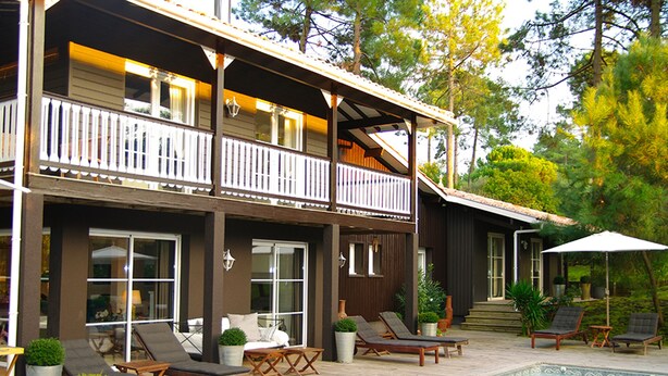 Ein zweistöckiges Haus mit Balkon, Swimmingpool und Sitzgelegenheit im Freien.