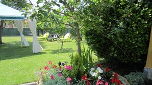 A garden with a wooden planter filled with colorful flowers, a grassy lawn, and a white gazebo in the background.