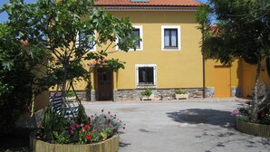 A yellow building with a tiled roof, a stone foundation, and a paved driveway.