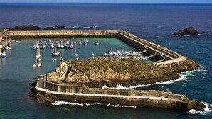 A coastal harbor with a fortified breakwater, numerous boats, and a clear view of the sea.