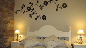 A bedroom with a stone wall, a bed with white bedding, and a floral wall decal.