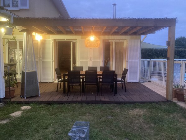 Un patio exterior con piso de madera, una mesa con sillas y una lámpara colgante.