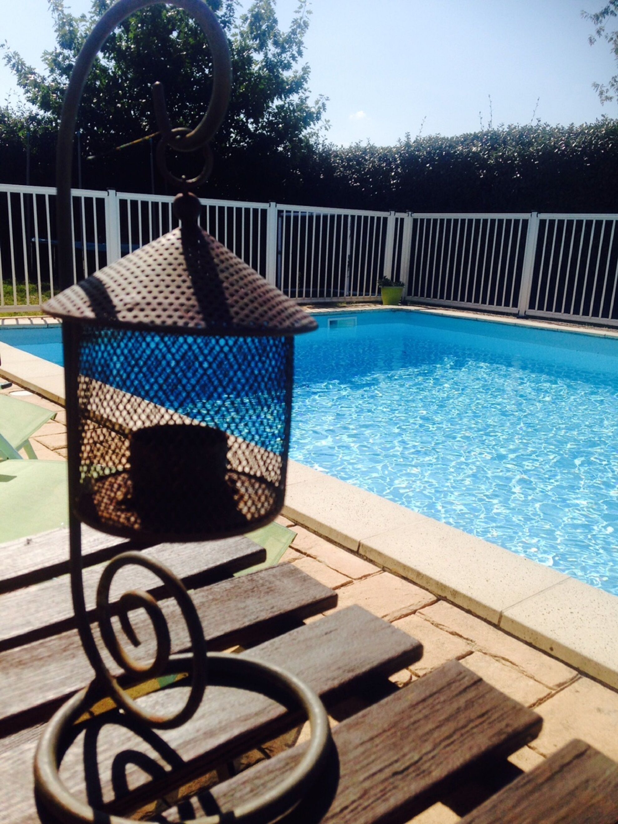 Ein Poolbereich mit einer hängenden Laterne, einer Holzterrasse und einem Pool.