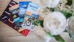 Guías de viaje y un folleto sobre bicicletas para vacaciones sobre una superficie de madera con rosas blancas.