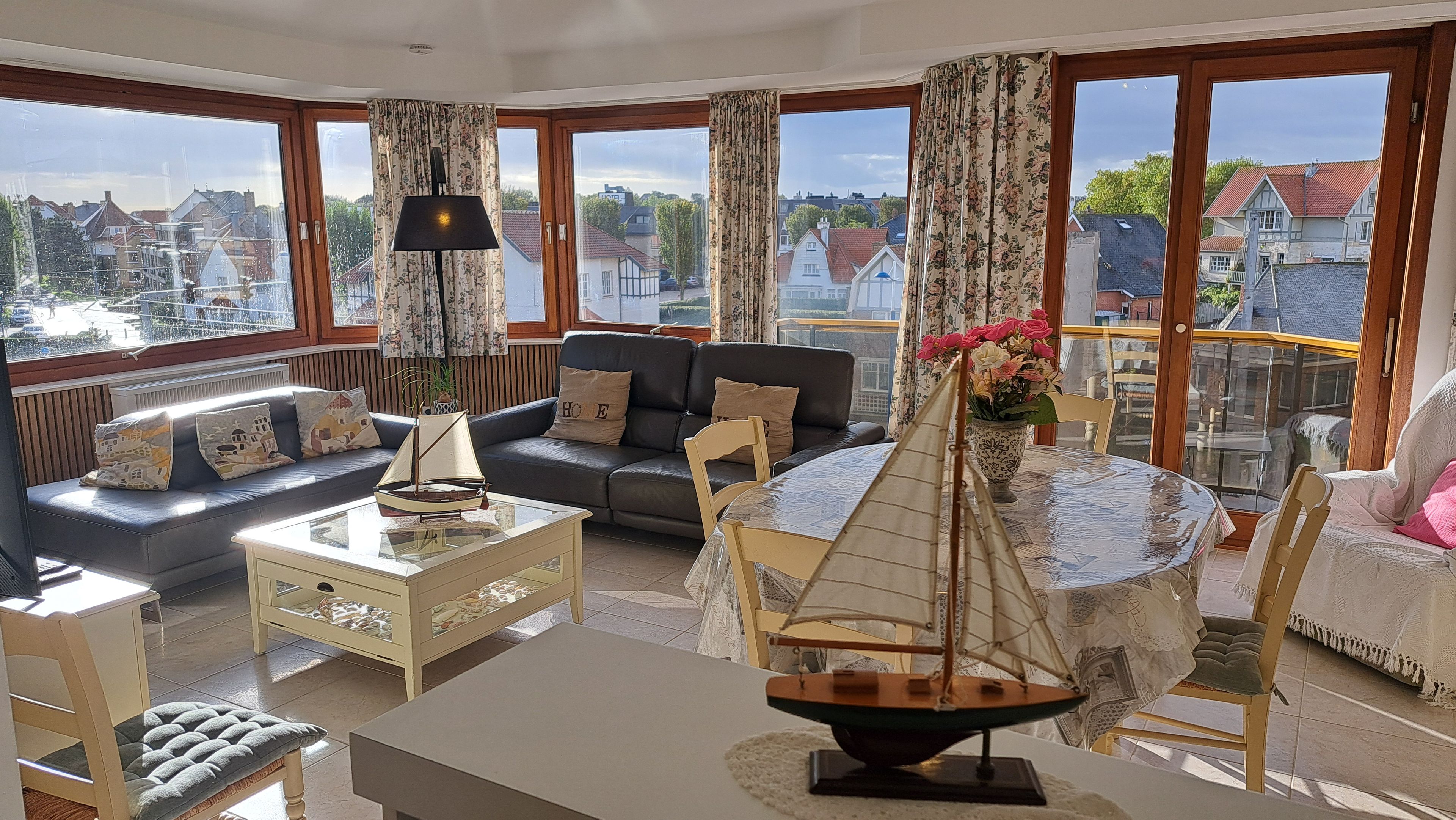 A spacious living room with a sofa, a coffee table, and a dining table with a sailboat model.