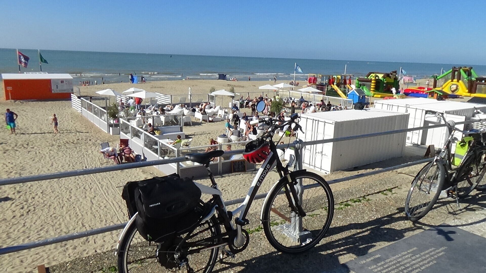 Eine Strandbucht mit einem Fahrrad neben einer Brüstung, einem weißen Gebäude und Strandstühlen.