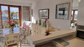 Un coin repas comprenant une table, des chaises, un vase de fleurs, une maquette de voilier et un tableau encadré accroché au mur.