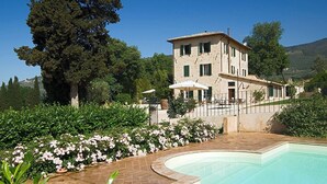 A two-story building with a pool, surrounded by lush greenery and a large tree. - Farmhouse holidays in Umbria, the green heart of Italy, amongst art and nature. (Spello)