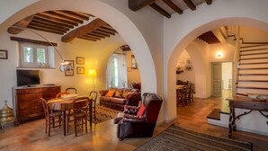 A spacious living area with a wooden dining table, leather armchairs, and a staircase with wooden beams. - Farmhouse holidays in Umbria, the green heart of Italy, amongst art and nature. (Spello)