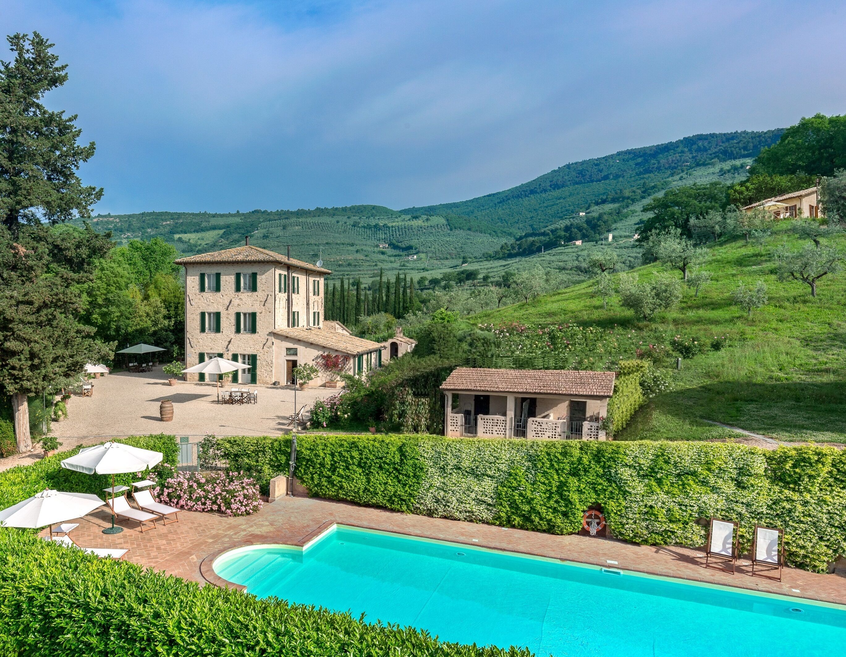 Une villa avec piscine, un espace salon extérieur et une vue sur des collines verdoyantes.