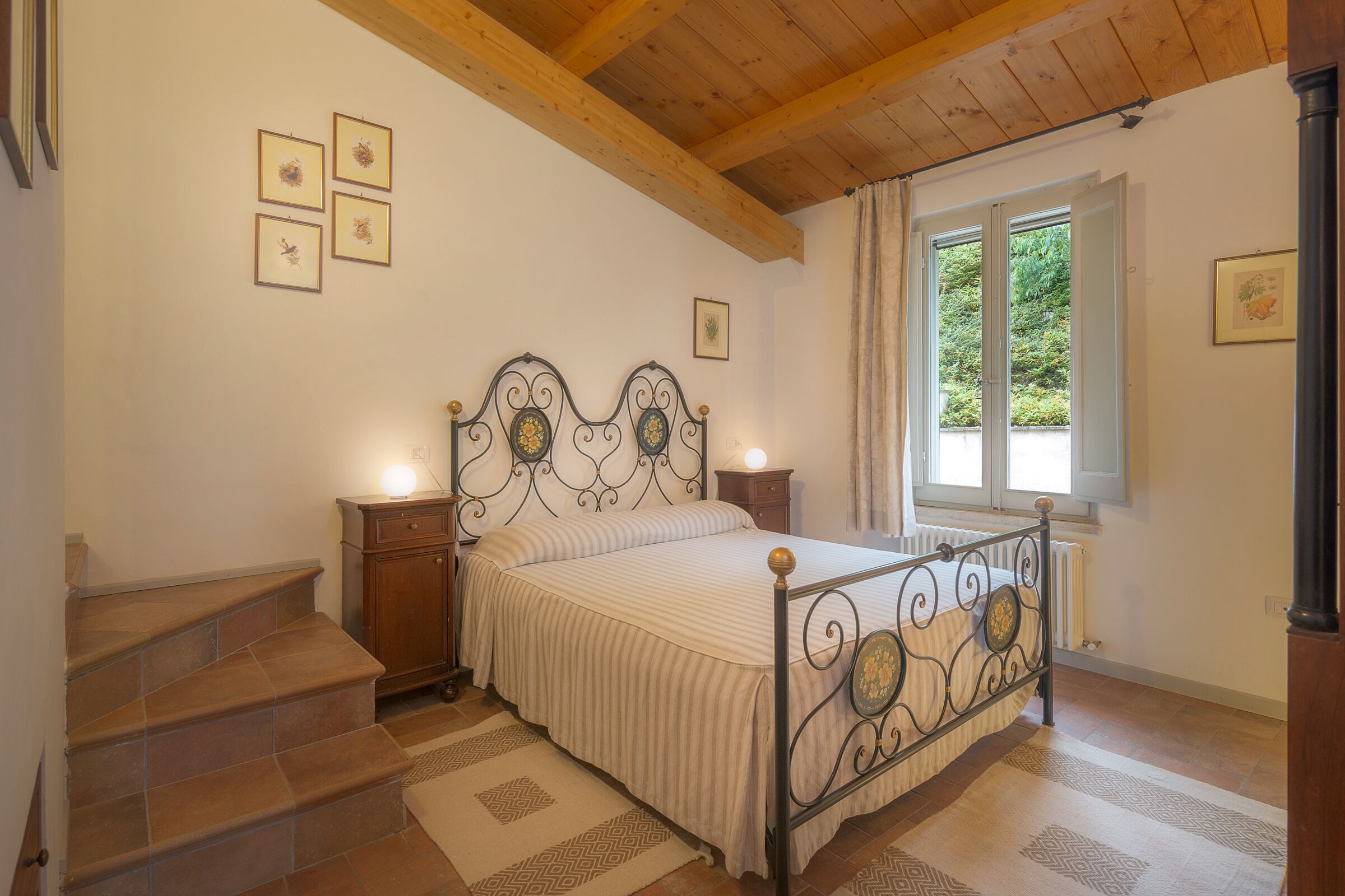 Un dormitorio con una cama, una mesita de noche, un ventanal y una escalera.