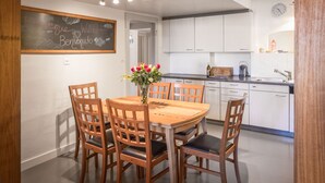 A modern kitchen with white cabinets, a wooden dining table with four chairs, and a chalkboard with 'Welcome' written on it.