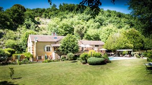 Une maison à deux étages avec une piscine, entourée d’une pelouse bien entretenue et d’arbres.