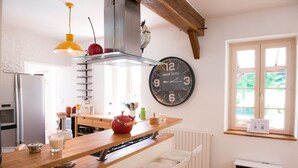 Une cuisine avec un plan de travail en bois, une bouilloire rouge, une horloge et une fenêtre donnant sur un beau paysage.